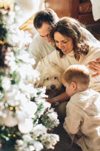 A joyful family gathers around a Christmas tree with their pet dog indoors.
