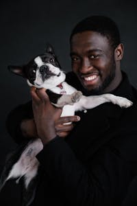A joyful moment of a man hugging his Boston Terrier puppy indoors.