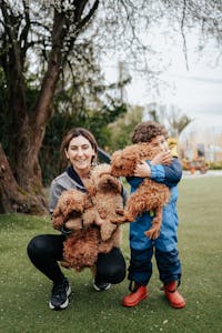 Mother and child play with poodles in a lush park setting. Joyful outdoor family moment.