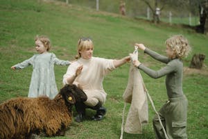 Mother and daughters enjoying a day outdoors with sheep at a farm, showcasing family bonding and nature.