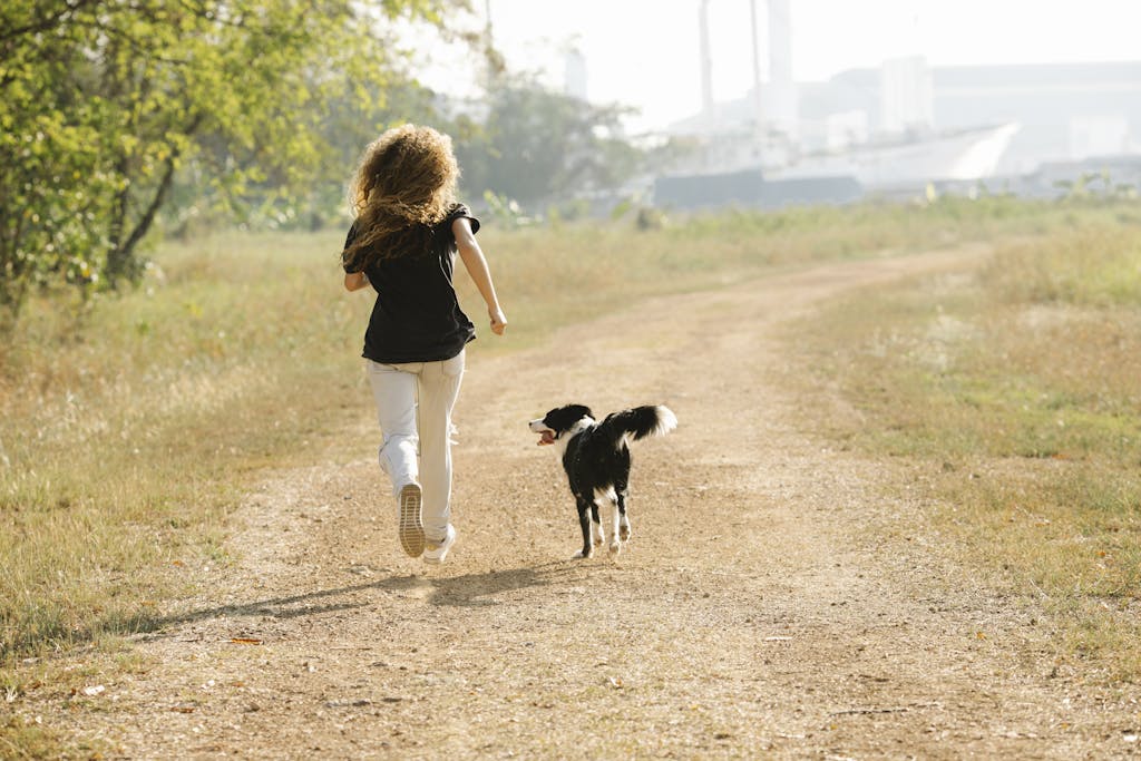A woman jogging with her dog along a sunny path in a park, showcasing outdoor fitness and companionship.