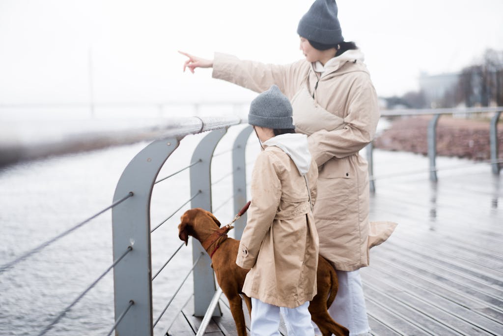 Mother and child in coats walking dog by the seaside, pointing at distant views.