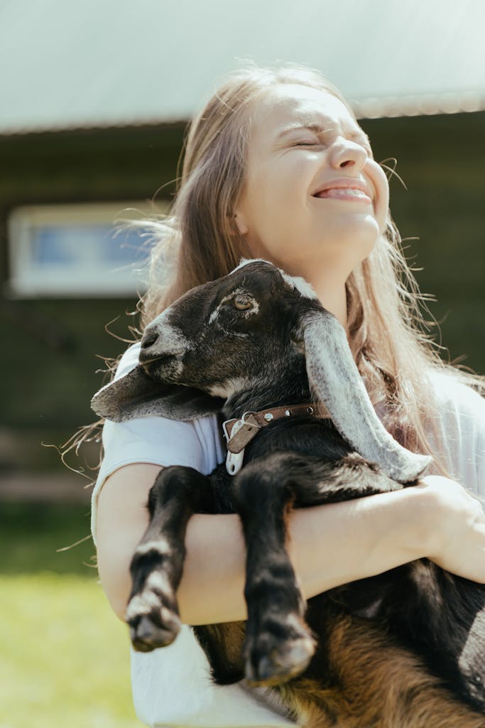 Young woman joyfully holding a goat on a sunny day at a rural farm. Perfect for lifestyle and nature themes.